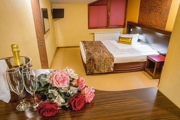A hotel room with a bed, bedside table, and a bouquet of flowers. - Eleganza Family Hotel (Sofia)