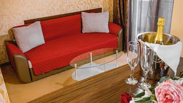 A hotel room with a red sofa, a glass table, a bottle of champagne, and a bouquet of flowers.