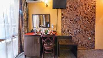 Una camera d'albergo con una scrivania, una sedia e un televisore a parete.