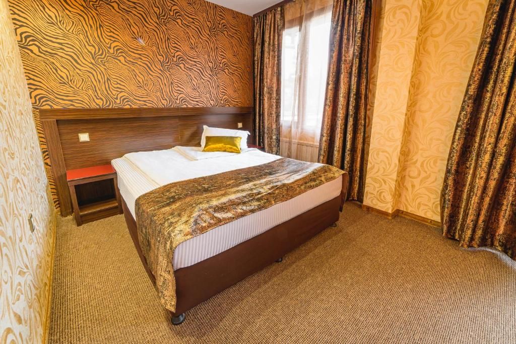 A hotel room with a large bed, a wooden headboard, a small bedside table, and patterned curtains.