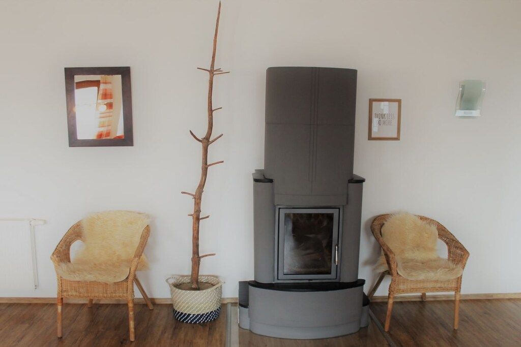 A room with a fireplace, two wicker chairs, a tall plant, and framed pictures on the wall.