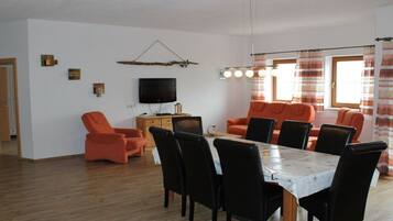 A living room with a dining area, a television, and a window with curtains.
