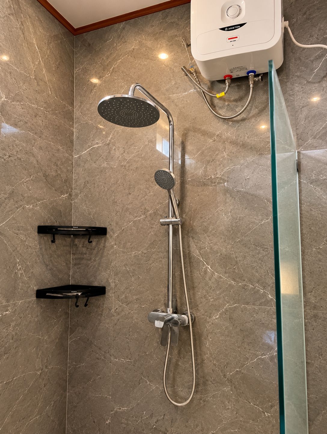 Une salle de bain moderne avec un sol en marbre, une douchette à main, un robinet mural et une paroi de douche en verre.