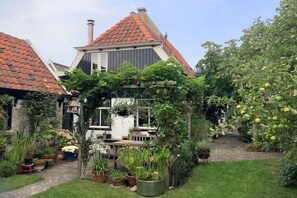 Ein Garten mit einer Pergola, Blumentöpfen und einem Weg, der zu einem Haus mit roten Ziegeldach führt.