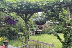 A garden with a pergola, a wooden bench, and various plants and flowers. - Holiday apartment with 2 bedrooms (Oudeschild)