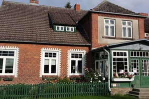 A two-story brick house with a green front porch and a small attached structure with windows. - Holiday apartment with 2 bedrooms (Neuenkirchen)