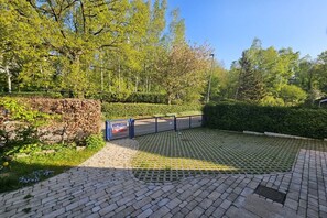A paved outdoor area with a metal fence, surrounded by greenery and trees. - Holiday home House Schiffchen (Sierksdorf)
