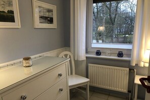 Ein Badezimmer mit einer weißen Heizung, einem Fenster mit Blick auf Bäume und einem weißen Stuhl.