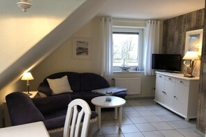 A cozy living area with a sofa, a small table, a television, and a cabinet. - Holiday apartment with 1 bedroom (Hohwacht)