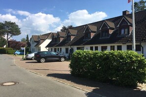 Eine Reihe traditioneller Häuser mit Satteldächern, einer gepflasterten Auffahrt und einer Hecke im Vordergrund.
