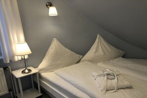 Un lit bien fait, avec du linge de lit blanc et des oreillers, une lampe de chevet et un radiateur.