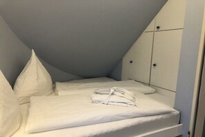 Ein ordentlich bezogenes Bett mit weißen Leinen und Kissen, ein gefaltetes Handtuch und ein Kleiderschrank mit zwei Türen.