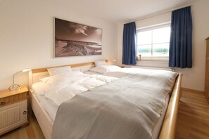 Ein Schlafzimmer mit einem großen Bett, einem Nachttisch, einem Fenster mit Vorhängen und einem Wandbild.