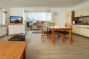 Eine moderne Küche mit Holzschränken, einem Esstisch mit Stühlen, einem Fernseher und Blick auf eine Brücke und Schiffe durch eine Glastür.