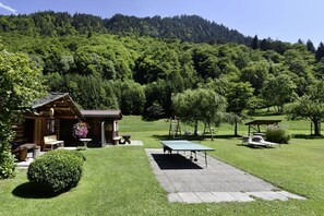 A rustic cabin with a patio area, surrounded by lush greenery and a forested hill. - Holiday apartment with 1 bedroom (Gortipohl)