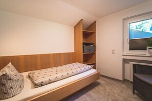 Ein kleines Schlafzimmer mit einem Einzelbett, einer eingebauten Ablage, einem Fenster mit Jalousien und einer Heizung.