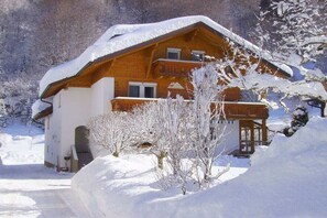 Una xalet de fusta amb un balcó, envoltat d'arbres coberts de neu i un cel serè.