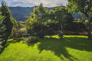 Ein üppiger Garten mit verschiedenen Bäumen und Sträuchern, einem gepflegten Rasen und einer bergigen Kulisse.