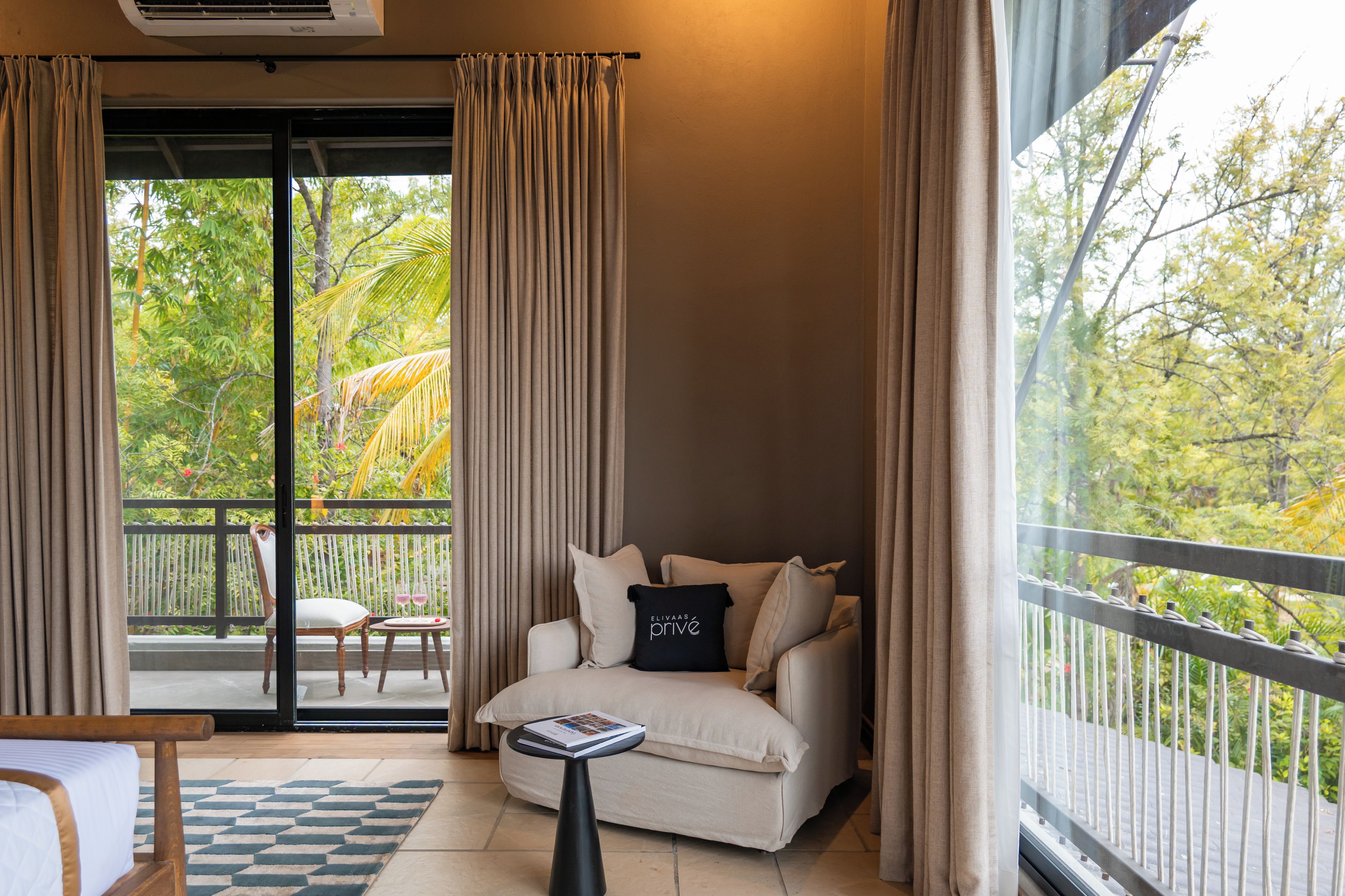 Ein Zimmer mit einer Couch, einem kleinen Tisch und Blick auf einen Balkon mit Vorhängen.
