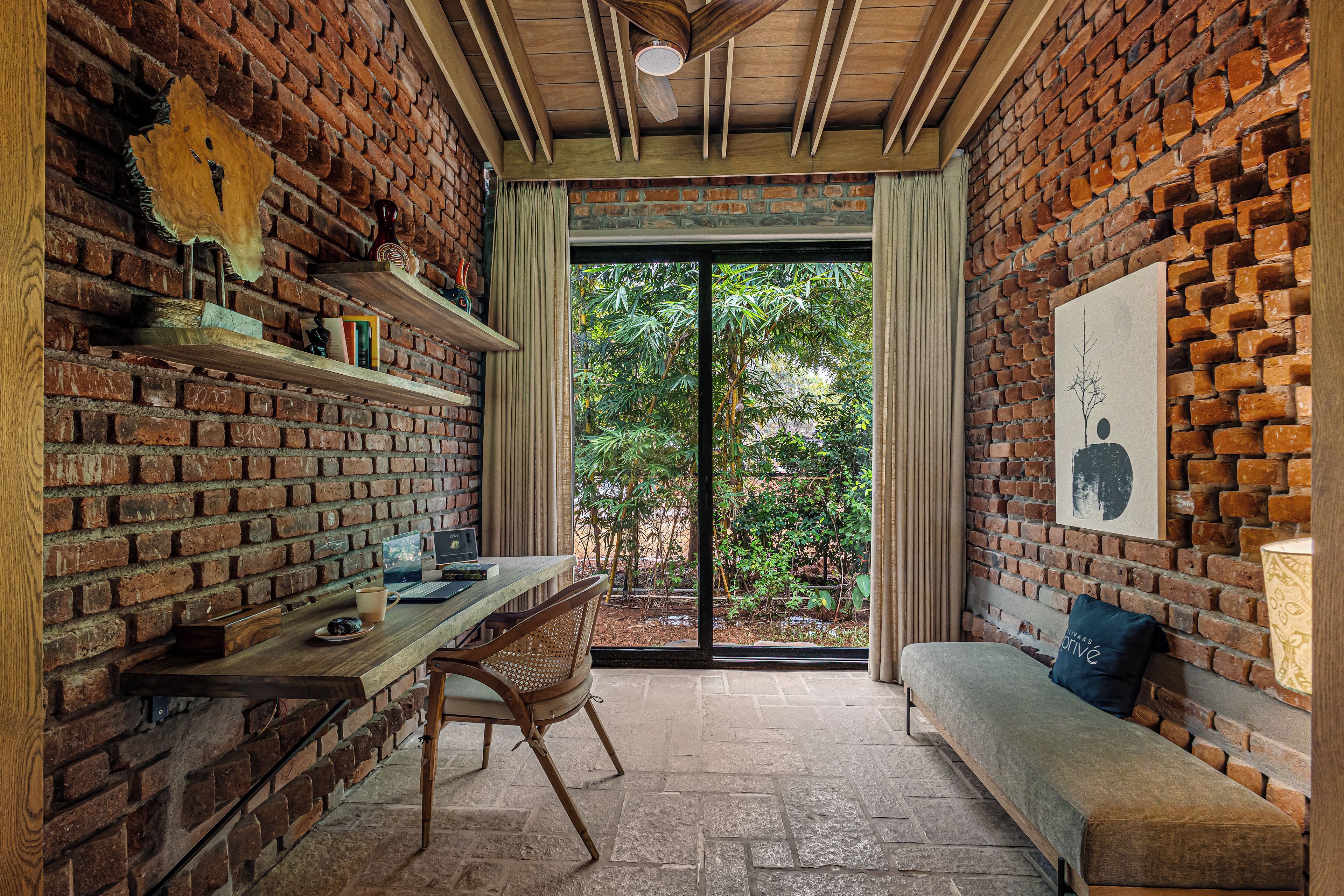 Una habitación con pared de ladrillo, una mesa de madera con una computadora portátil, una silla y un banco.