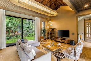 A spacious living room with a large TV, comfortable seating, and a view of a lush garden.