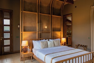 Habitación de hotel con una cama grande, dos mesitas de noche, cabecera de madera, estante empotrado y puerta con paneles de vidrio.