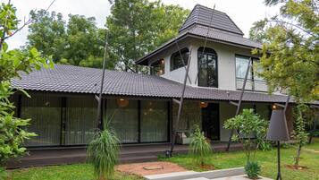 Une maison à deux étages, avec un toit recouvert de tuiles, de grandes fenêtres et un jardin avec des marches menant à l’entrée.
