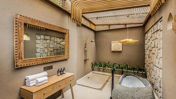 Un baño con tocador de madera, lavamanos de piedra, ducha y bañera de piedra.