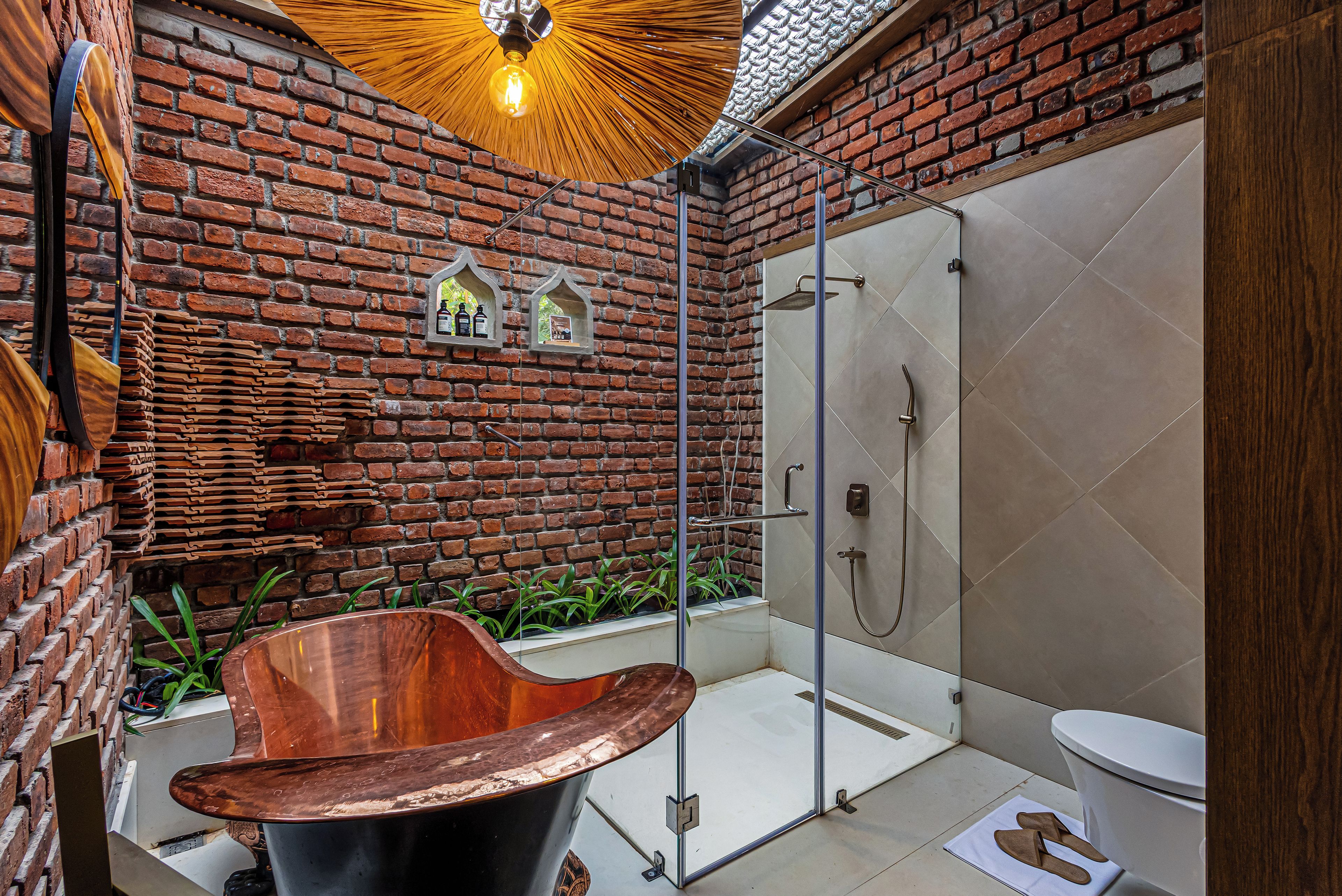 A bathroom with a brick wall, a glass shower enclosure, and a copper bathtub.
