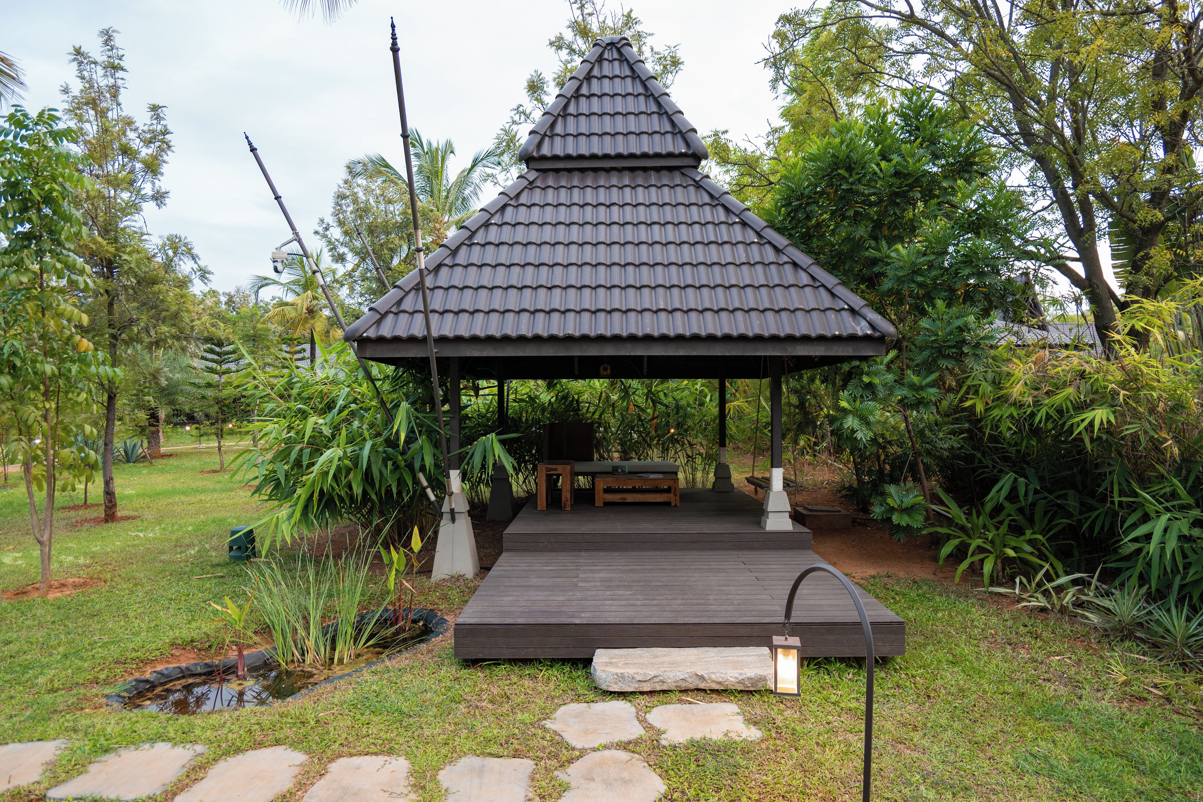 Un gazebo con tetto in tegole, una panca in legno e un vialetto in pietra che vi conduce.