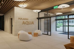 Ein modernes Interieur mit einem Schild, auf dem 'POLANKI AQUA' steht, und einem Empfangsbereich mit einer Glastür, die nach draußen führt.
