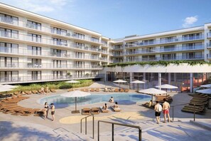 Ein modernes Hotel mit mehreren Balkonen, einem zentral gelegenen Schwimmbad und Liegestühlen.