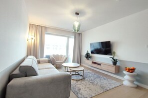 Ein modernes Wohnzimmer mit einer Couch, zwei Sesseln, einem Fernseher und einem kleinen Tisch.