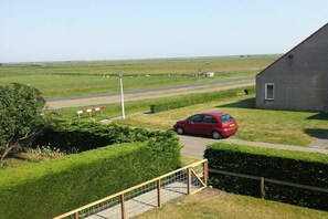Entorno rural con un coche rojo estacionado cerca de un edificio, una carretera y campos abiertos.