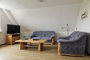 A living room with a television, a sofa, a chair, and a coffee table. - Holiday apartment with 1 bedroom (Nes Ameland)