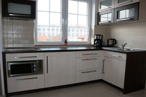 A kitchen with a built-in oven, a window with lace curtains, and a coffee maker. - Villa Guta, Apartment 2 (Rowy  Polen)