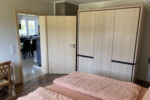 A bedroom with a bed, a wardrobe, and a dining area visible through an open door. - Villa Guta, Apartment 2 (Rowy  Polen)