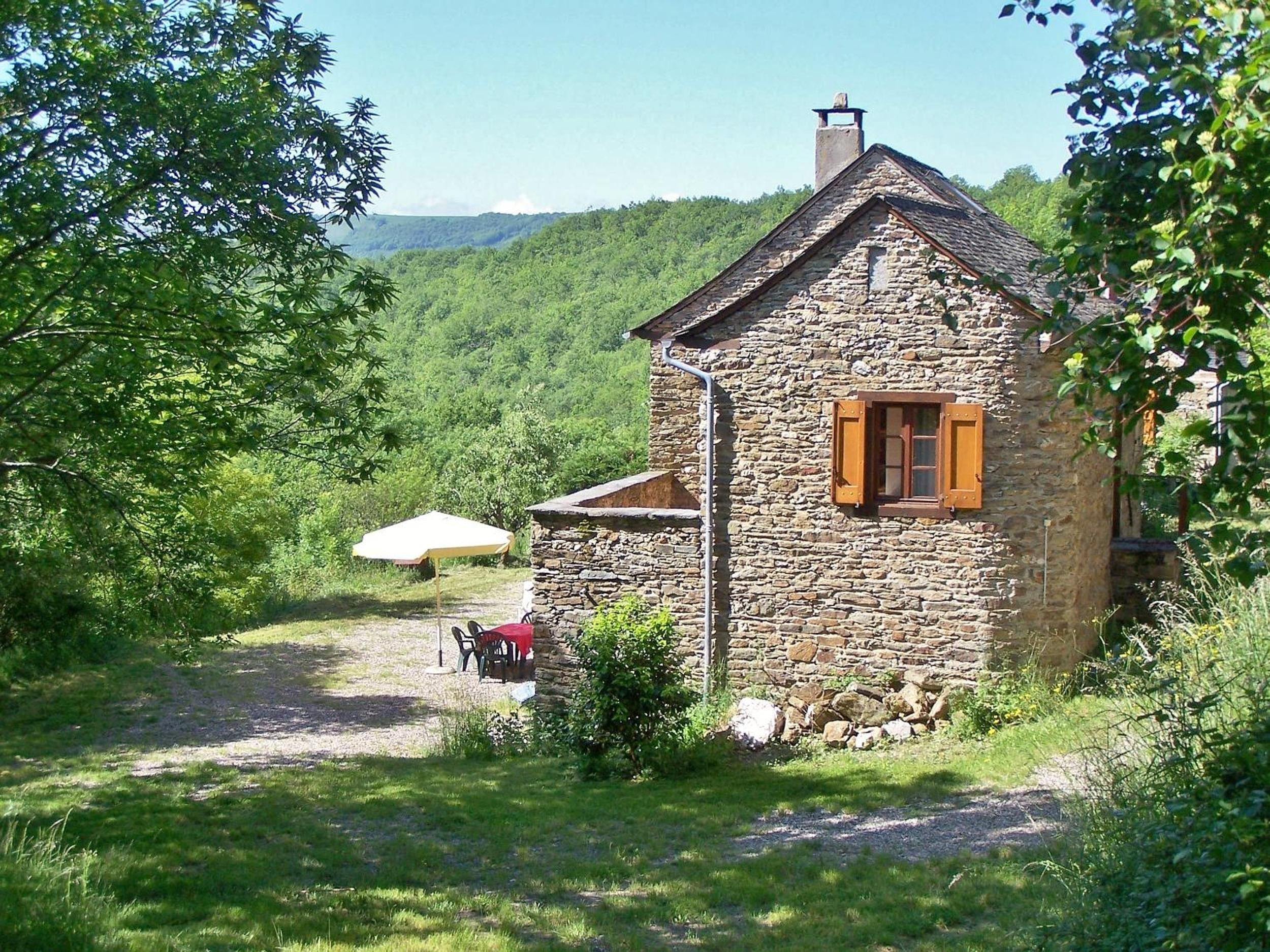 Ein Steinhaus mit Schornstein, einer kleinen Veranda und einem Tisch mit Stühlen davor.