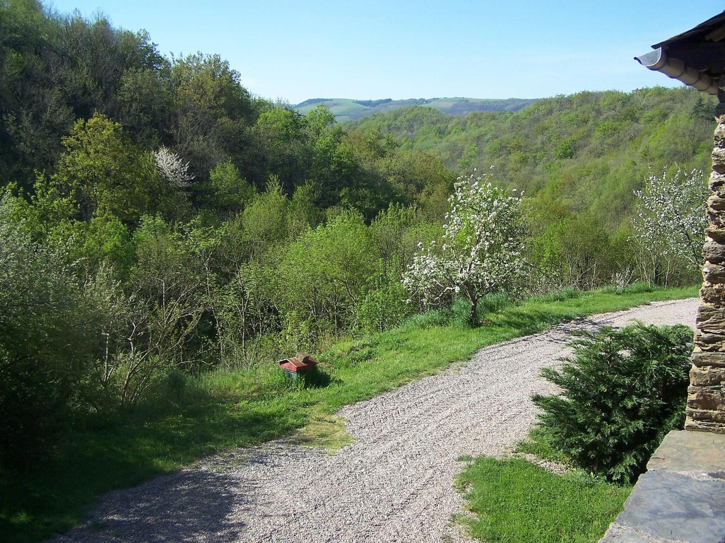 A gravel path leading through a lush green landscape with trees and a stone building on the right.