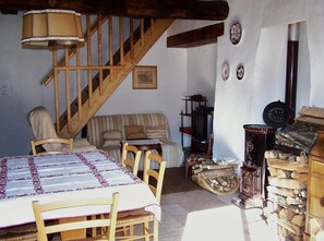 Un ambiente rustico con una scala in legno, un divano, un tavolo con tovaglia fantasia e un camino.