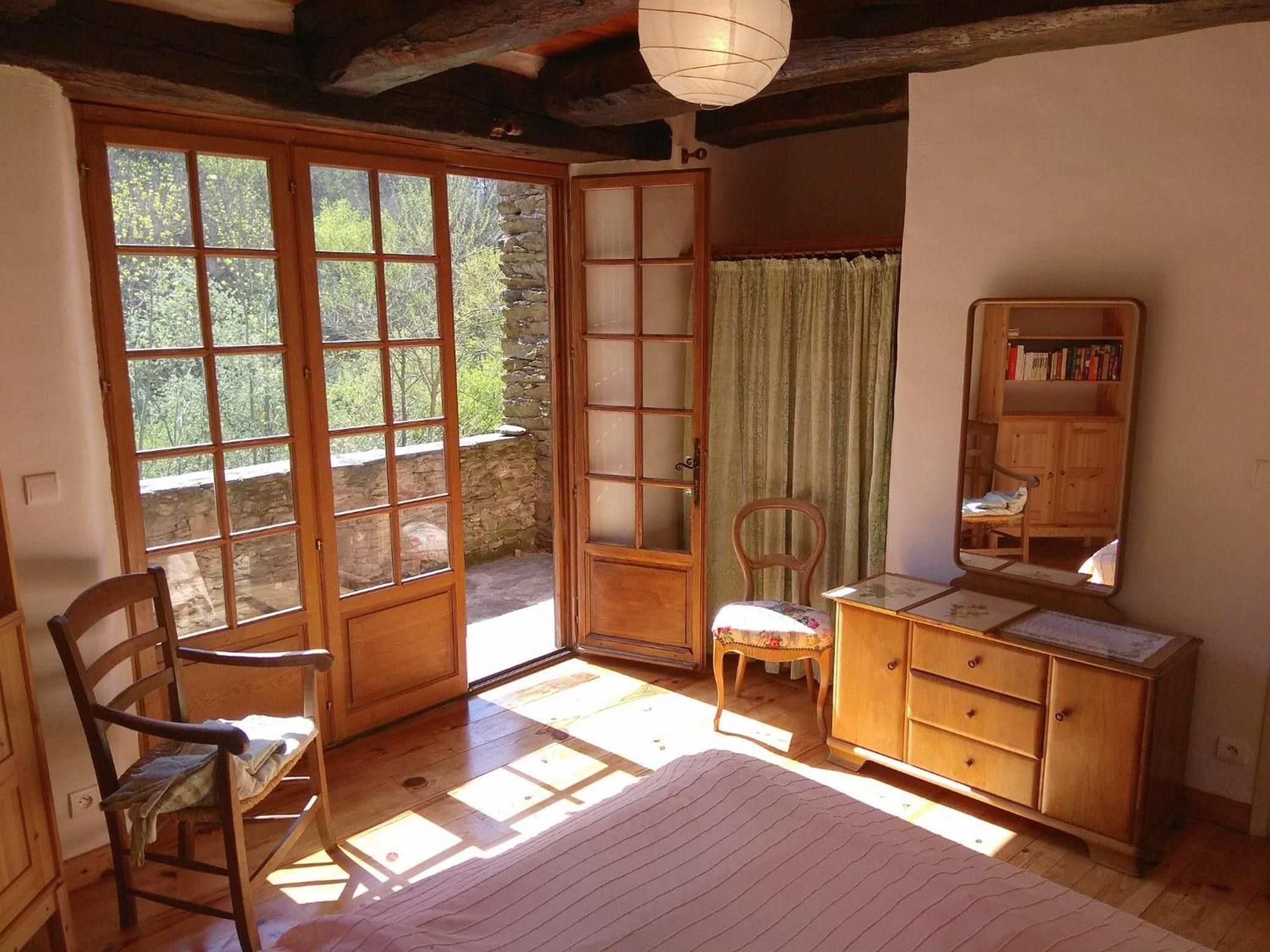 Ein Zimmer mit einem Holzstuhl, einem Holzschrank und einem großen Fenster mit Blick auf Bäume.