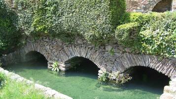 A stone bridge with arches over a clear water channel, surrounded by greenery.