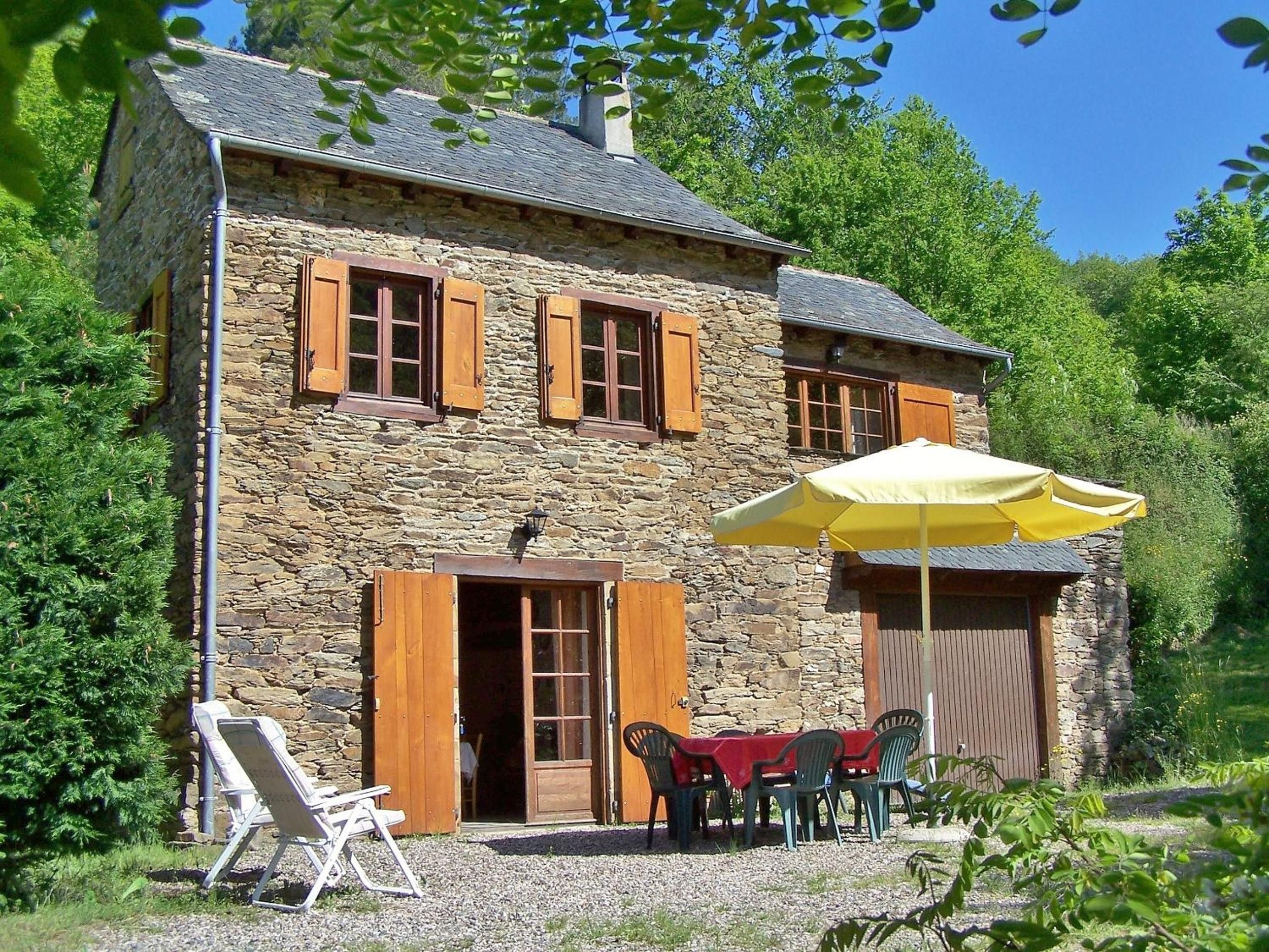 Ein Steinhaus mit Holztür und -fenstern, einer überdachten Außenbestuhlung und einem Kiesgrund.