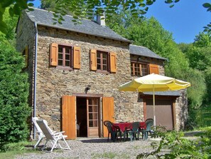 Un edificio in pietra con una porta e finestre in legno, una zona relax all'aperto coperta e un terreno sterrato.