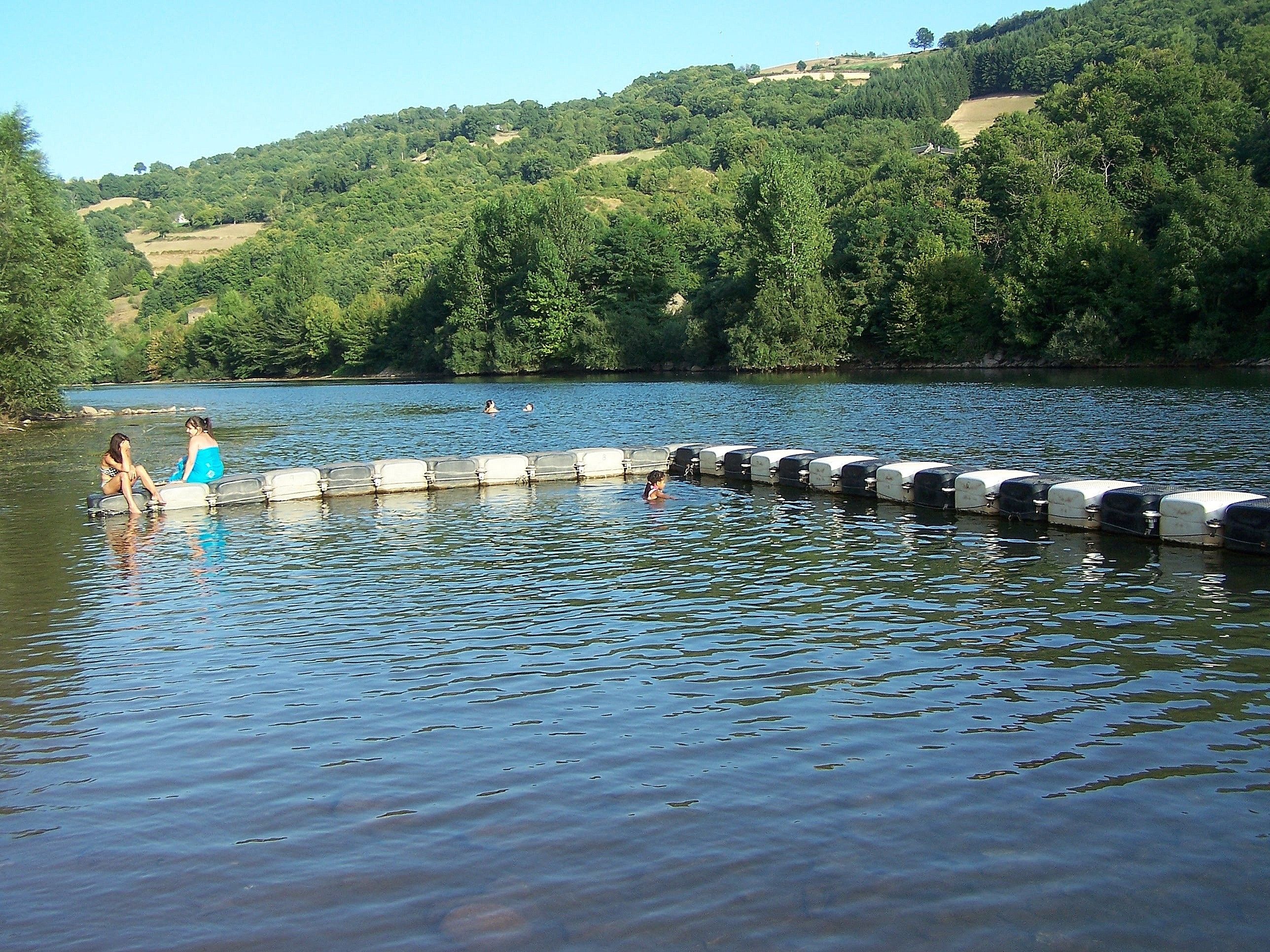 Un lago con una fila de barreras de hormigón y dos personas sentadas al borde.