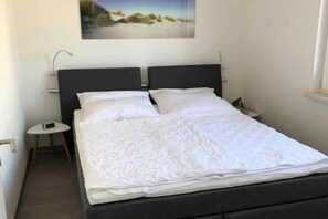 A single bed with a dark headboard, white bedding, and a small bedside table with a lamp. - Holiday apartment with 1 bedroom (Gelbensande)