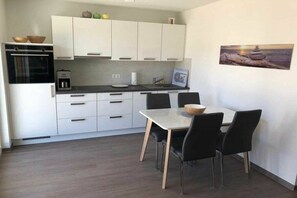 A modern kitchen with white cabinets, a built-in oven, and a dining area with a table and chairs. - Holiday apartment with 1 bedroom (Gelbensande)