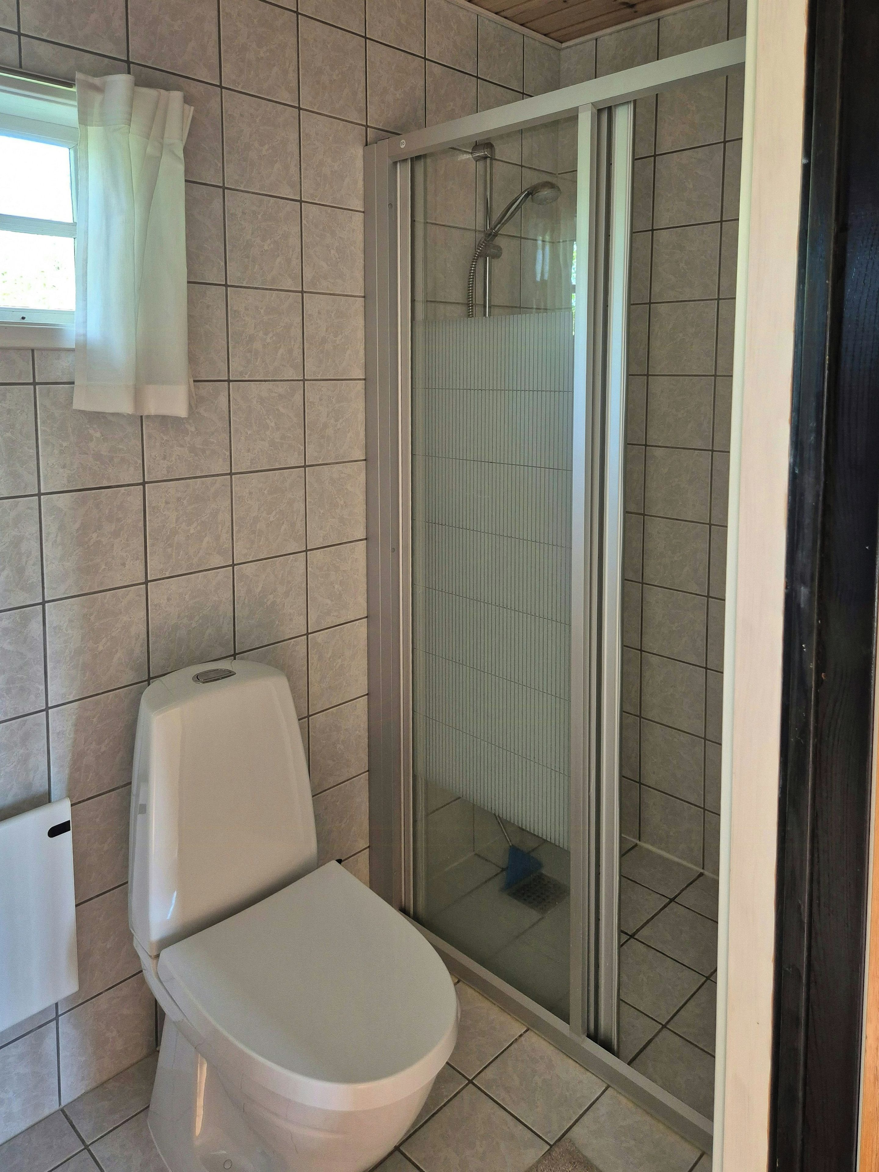 A bathroom with a toilet, a shower enclosure, and a window with a curtain.