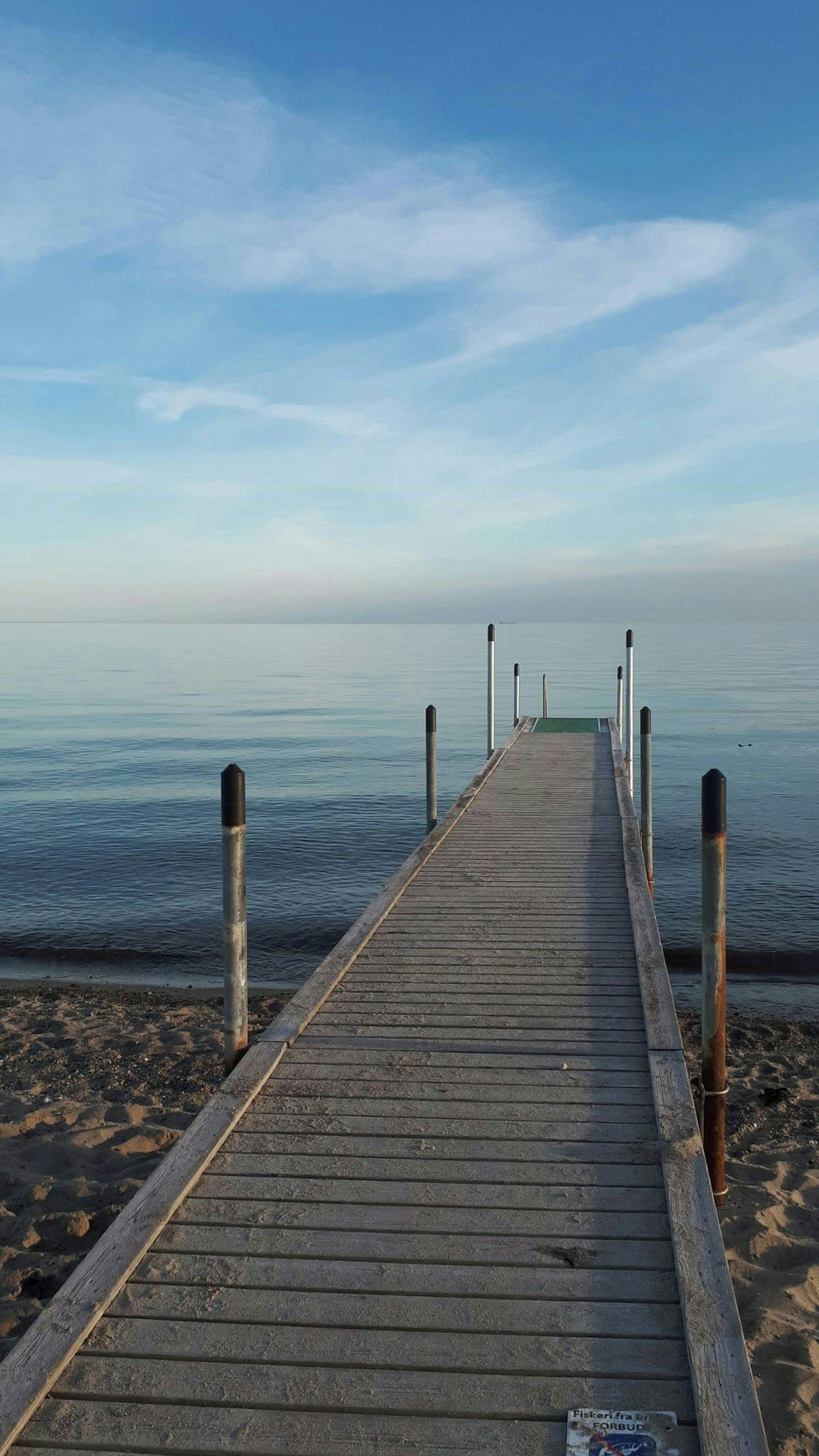 A wooden pier extending into calm water with a clear sky above.