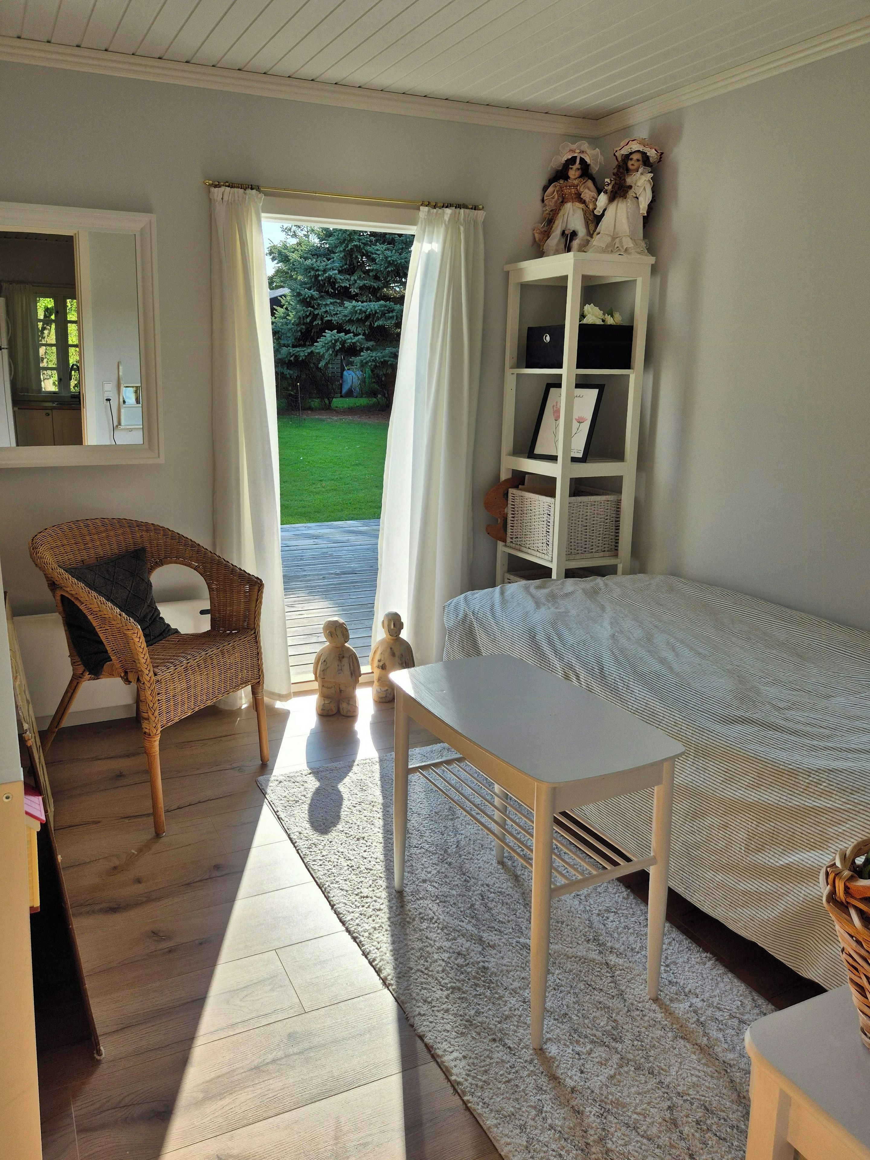 Quarto com cama, poltrona, mesinha, prateleira com objetos decorativos e vista para o exterior.
